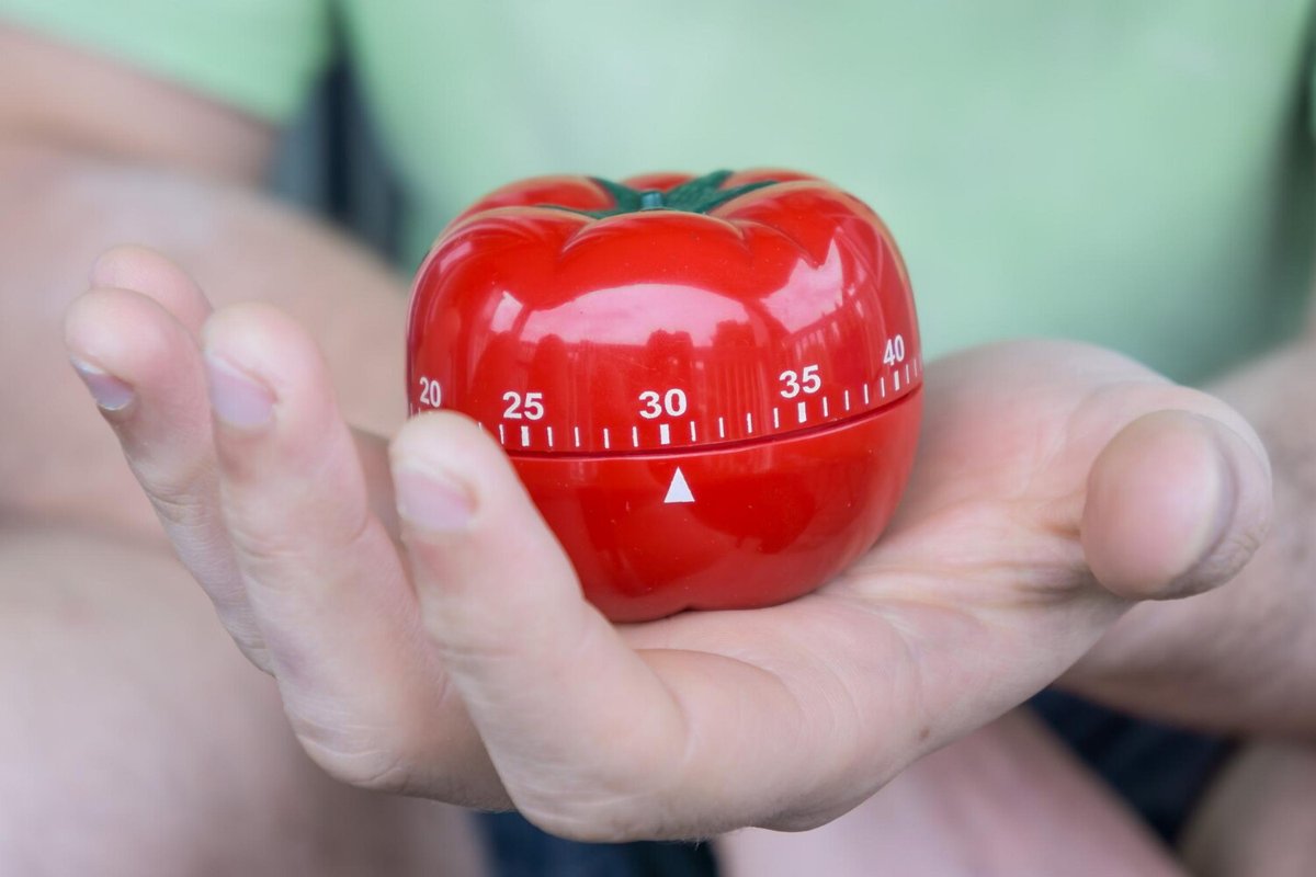 Человек держит в руках таймер в виде красного помидора