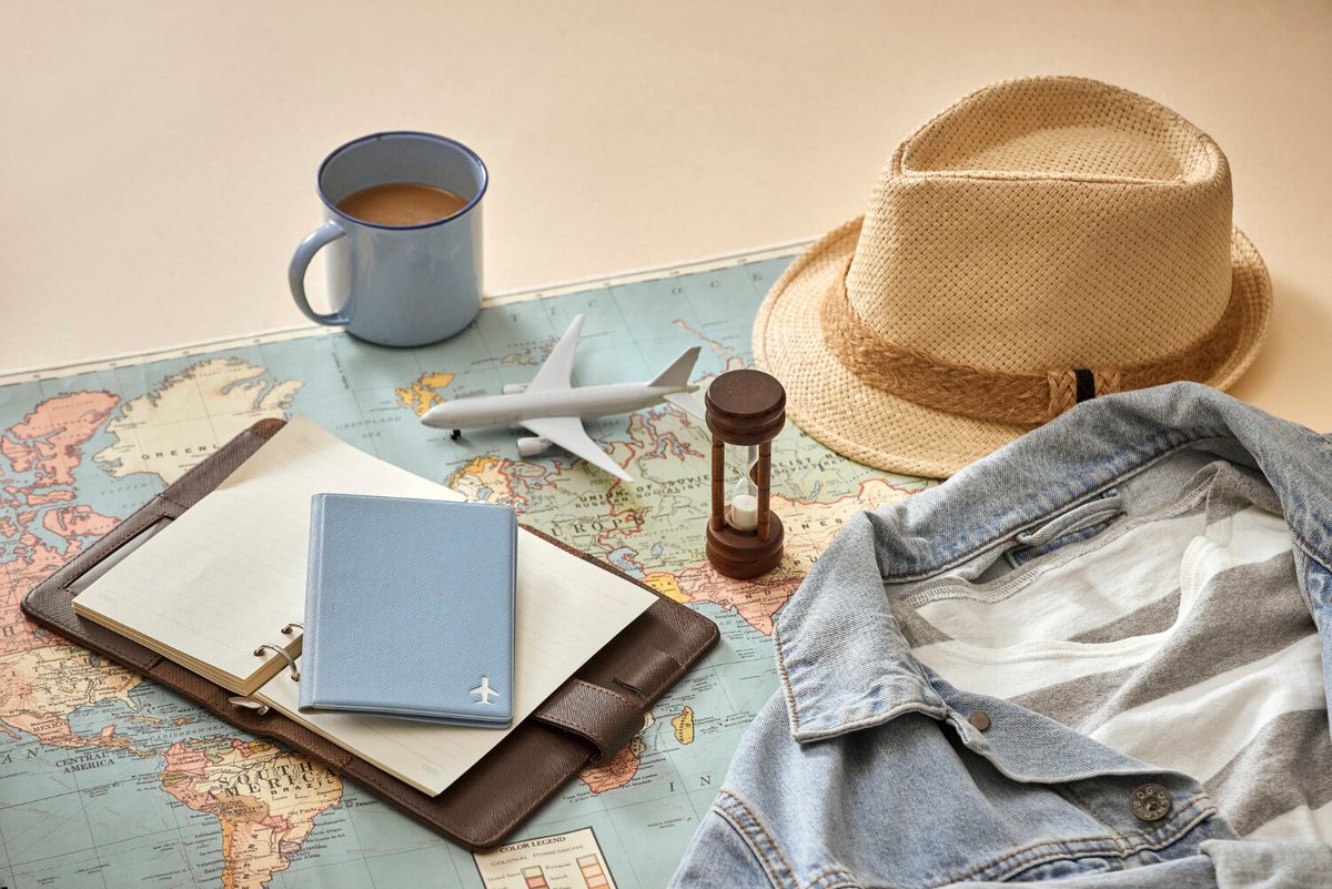 Композиция из карты мира, блокнота, кружки, шляпы, джинсовки, игрушечного самолёта и песочных часов