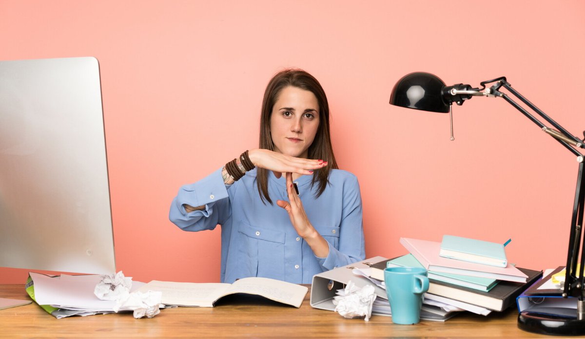 Девушка за рабочим столом руками показывает жесть "таймаут"